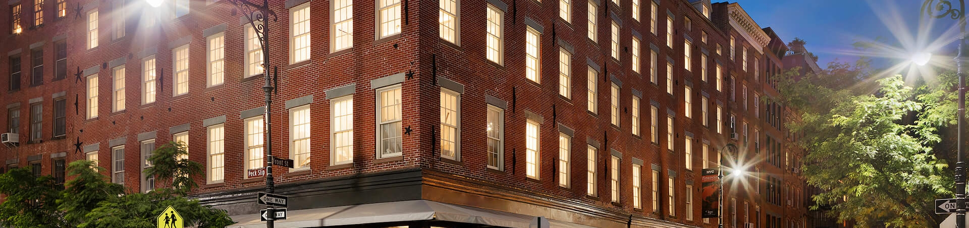 exterior shot of a brick building with lights on in rooms on a cobblestone street