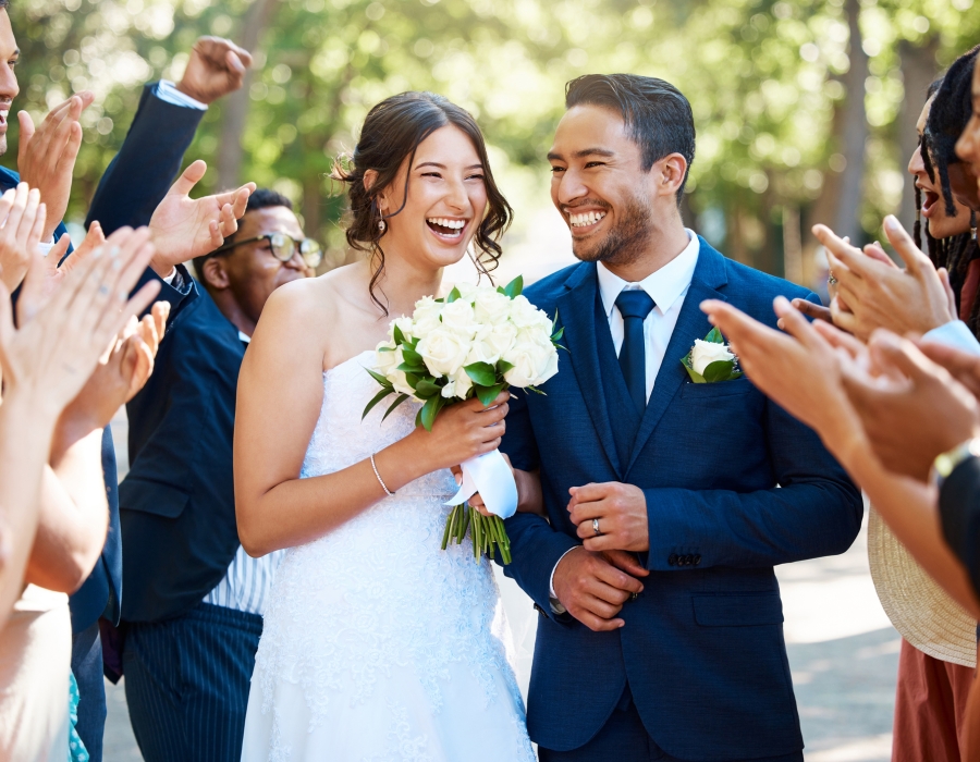 Wedding guests clapping hands as the newlywed couple walk down the aisle. Joyful bride and groom walking arm in arm after their wedding ceremony